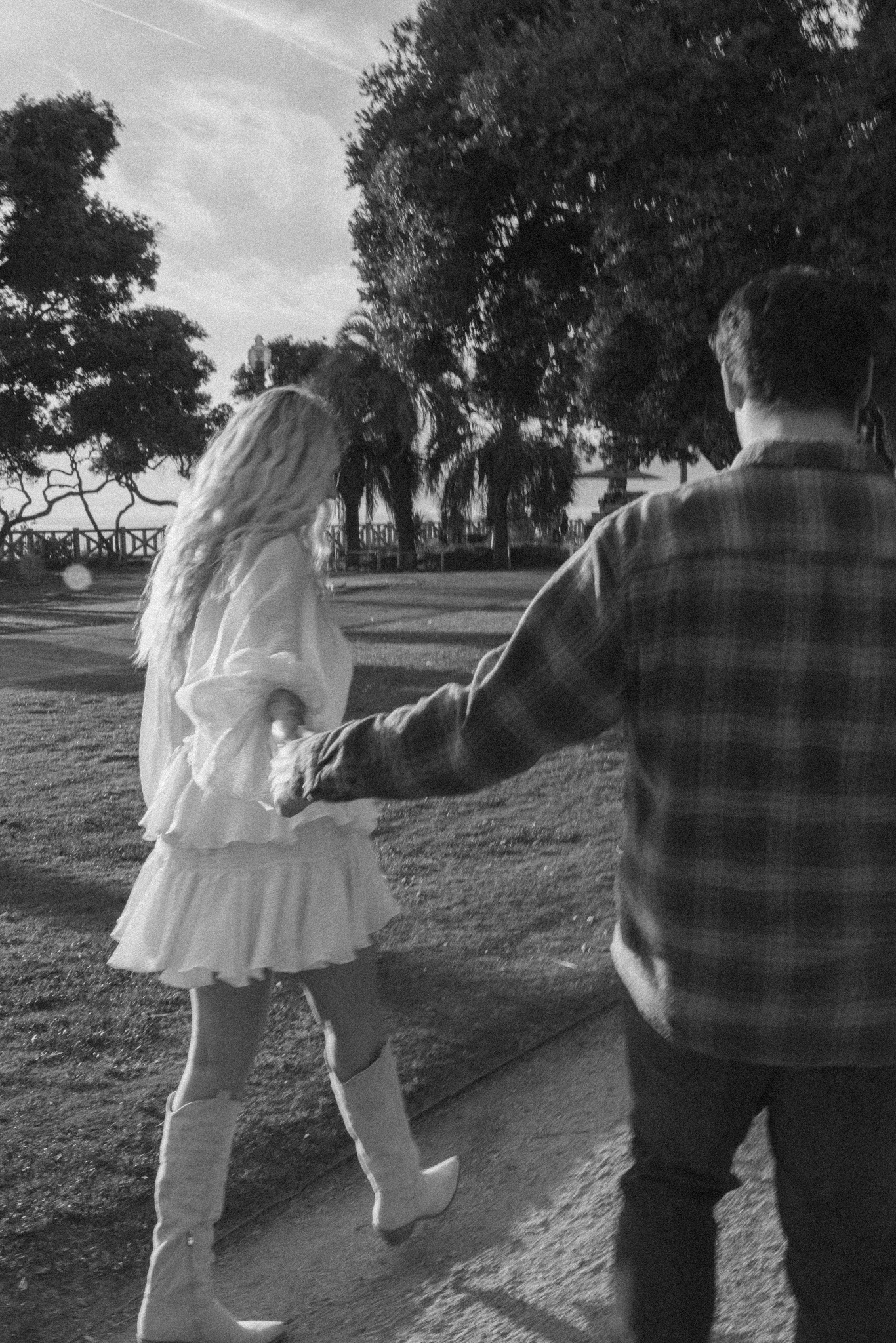 Jamie and Sean walking hand in hand through a park, in black and white