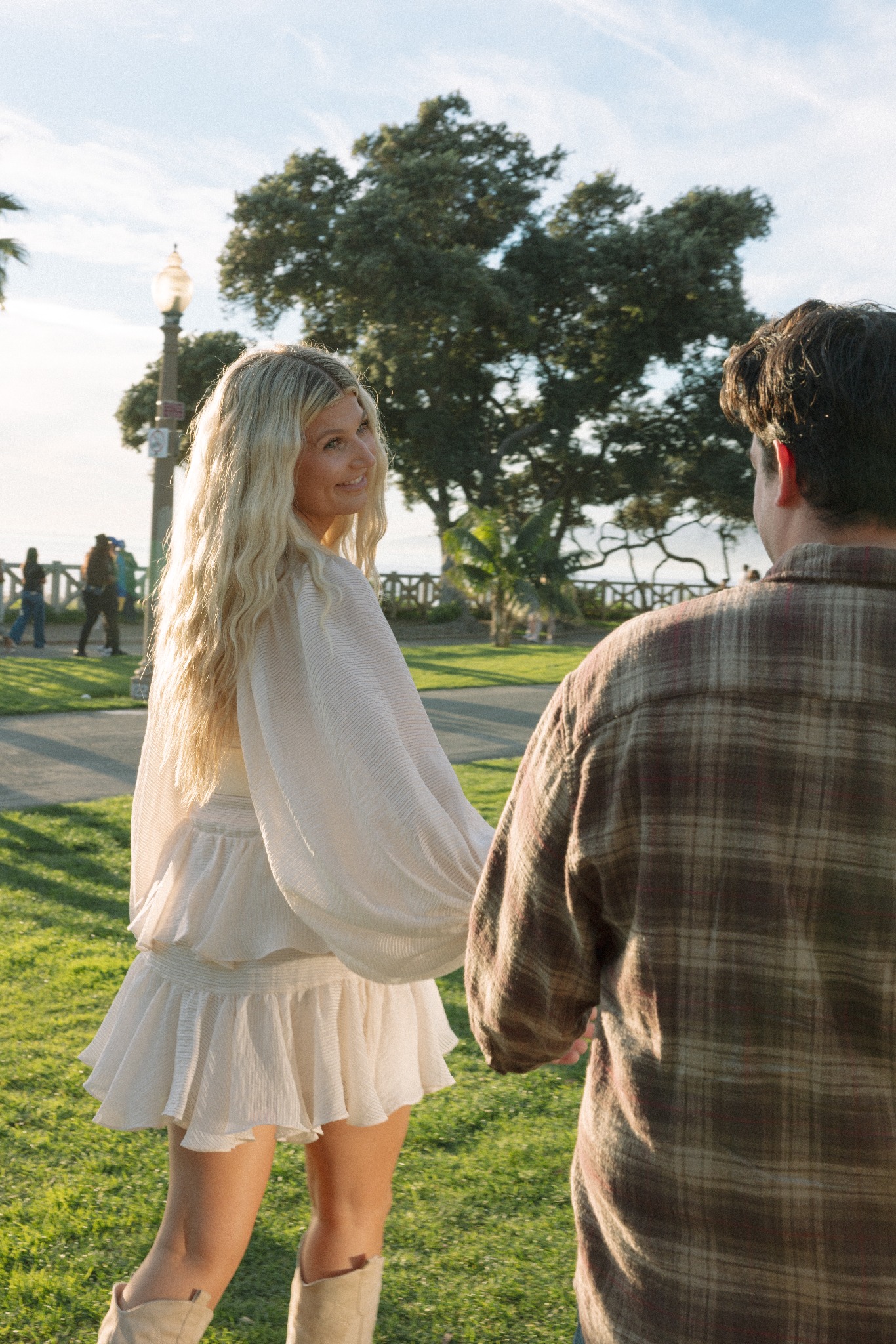 Jamie glancing back over her shoulder while holding Sean's hand under the trees